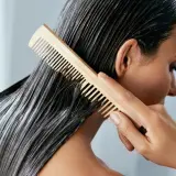 Frau kämmt nasses Haar mit Conditioner. Was ist Conditioner? Es macht das Haar weich und glänzend.
