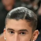 Nahaufnahme eines Mannes mit glatt zurückgekämmtem Haar und einem **low fade** Haarschnitt. Er trägt einen Perlenohrring.