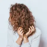 Frauen mit einer voluminösen Dauerwelle, die ihre Hände durch die Locken gleiten lassen.