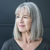 Porträt einer Frau mit stilvollen grauen Haaren, die nachdenklich zur Seite blickt.