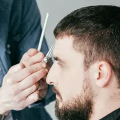 Ein Mann bekommt einen Caesar Cut. Der Friseur schneidet ihm mit einer Schere die Haare.