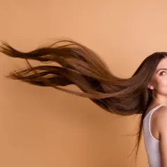 Frau mit langen, braunen Haaren, die im Wind wehen. Sie lächelt und blickt zur Seite.