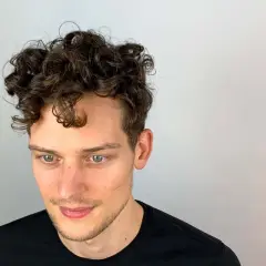Junger Mann mit vollen, dunklen Locken. Ein Beispiel, wie bekommt man locken jungs für einen coolen Look.
