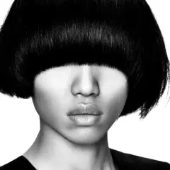 Ein Gesicht mit einem markanten **bowl cut** und dunklem Haar, das die Augen verdeckt. Die Lippen sind leicht geöffnet.