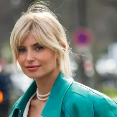 Blonde Frau mit soft curtain bangs, trägt eine türkise Lederjacke und Perlenkette.