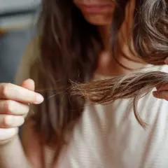 Frau prüft ihre fettigen Haare nach einem Tag. Die Strähnen kleben zusammen und wirken glanzlos.