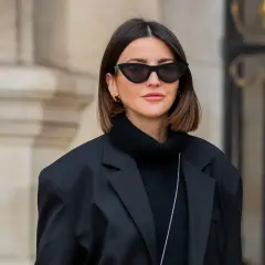 Frau mit langem Bob und Curtain Bangs, glatte Haare, trägt schwarzen Rollkragenpullover und Oversize-Blazer.