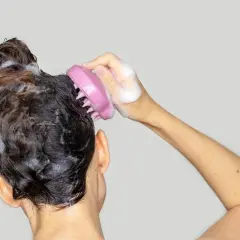 Eine Hand mit einem rosa Silikon-Haarwaschgerät massiert die nasse, schaumige Kopfhaut.
