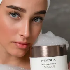 Frau mit Handtuch auf dem Kopf hält eine NEWSHA Haarmaske mit Schaum. Die Anwendung der Haarmaske verspricht Pflege.