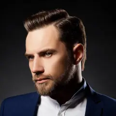 Ein Mann mit Bart und einem eleganten Seitenscheitel, gekleidet in einem blauen Anzug.