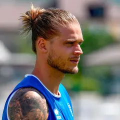 Ein Mann mit einem lässigen **man bun ohne bart**, trägt ein blaues Trikot. Sein Blick ist nach rechts gerichtet.