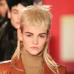 Model mit modernem Mullet-Haarschnitt, braunem Rollkragenpullover und Lederjacke. Goldene Ohrringe und auffälliger Ohrschmuck.