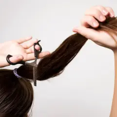 Frau schneidet sich mit einer Effilierschere die Haare, um einen Stufenschnitt selber zu schneiden.