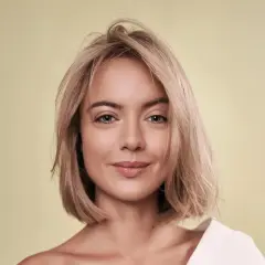 Porträt einer Frau mit blondem Haar und einem sanften Lächeln. Ihr Haar ist kurz geschnitten, wie ein **calligraphy cut**, und fällt locker um ihr Gesicht.