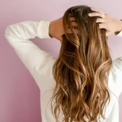 Frau mit langen, welligen 2a Haaren, die sie mit den Händen im Nacken hält.