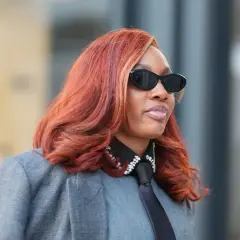Frau mit feurigem Haar, das eine der aktuellen Haarfarben widerspiegelt, trägt Sonnenbrille und grauen Blazer.