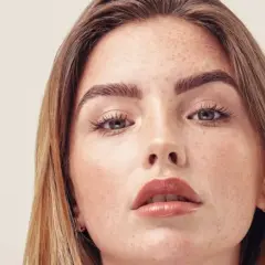 Nahaufnahme einer jungen Frau mit Sommersprossen und dunkelblond hellbraunen Haaren, die sanft über ihre Schultern fallen.