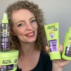 Frau mit lockigem Haar präsentiert die Garnier Fructis Locken Methode Produkte: Shampoo, Pre-Shampoo und Feuchtigkeits-Spray für definierte Locken.