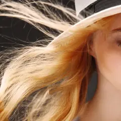 Ein Mädchen mit feinen Haaren, die im Wind wehen, trägt einen Hut.