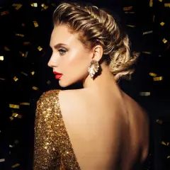 Elegante Frau mit aufwendiger Hochsteckfrisur, perfekt für Silvester-Frisuren. Goldglitzerndes Kleid und Konfetti im Hintergrund.