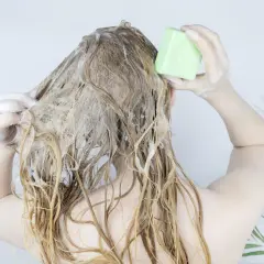 Frau wäscht sich die Haare mit einem festen Shampoo-Riegel. Die Herstellung von Shampoo kann so einfach sein.