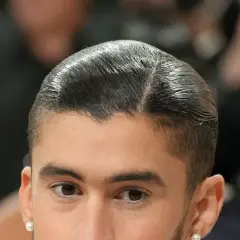 Nahaufnahme eines Mannes mit glatt zurückgekämmtem Haar und einem **low fade** Haarschnitt. Er trägt einen Perlenohrring.