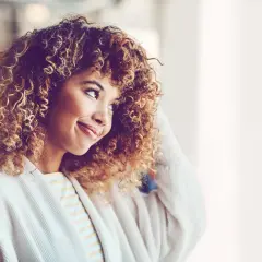 Lächelnde Frau mit voluminösen, stufig geschnittenen naturlocken frisuren, die ihr Gesicht umrahmen.