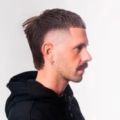 Mann mit einem flauschigen Edgar-Haarschnitt, der nach rechts blickt. Der Schnitt hat einen kurzen Pony und einen längeren Nacken.