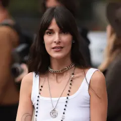 Frau mit dunklem Haar und Curtain Bangs, die eine weiße Tanktop und Chanel-Schmuck trägt.