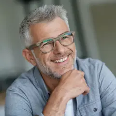 Lächelnder Mann mit Brille und grauem Haar, ein Beispiel für moderne herren frisuren ab 50.