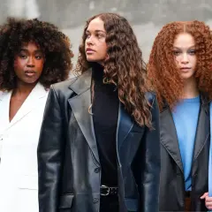 Drei Frauen mit voluminösen Locken, die sich fragen, wie oft locken waschen. Eine trägt Weiß, die andere Schwarz und die dritte Blau.