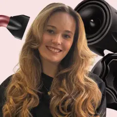 Lächelnde Frau mit voluminösen, welligen Haaren, die durch einen Dyson-Haartrockner und schwarze Aufsätze betont werden. Die Konturen der Haare sind perfekt gestylt.