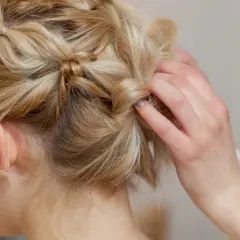 Eine Hand formt mittellange hochgesteckte Haare zu einem kunstvollen Zopf.