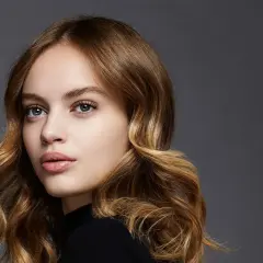 Porträt einer jungen Frau mit welligem, dunkelblondem Balayage-Haar, das sanft um ihr Gesicht fällt.