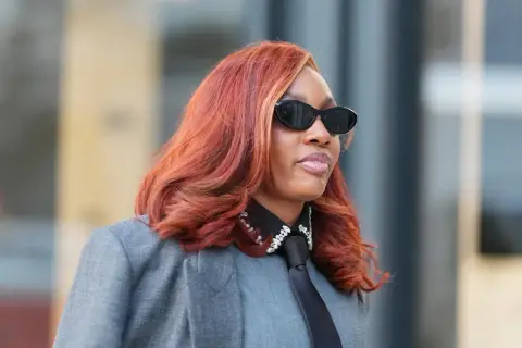 Frau mit feurigem Haar, das eine der aktuellen Haarfarben widerspiegelt, trägt Sonnenbrille und grauen Blazer.