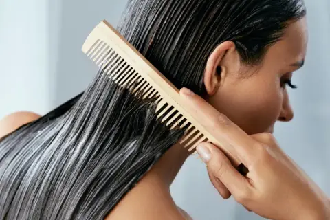 Frau kämmt nasses Haar mit Conditioner. Was ist Conditioner? Es macht das Haar weich und glänzend.