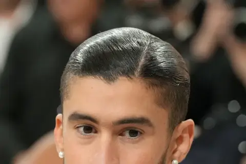 Nahaufnahme eines Mannes mit glatt zurückgekämmtem Haar und einem **low fade** Haarschnitt. Er trägt einen Perlenohrring.