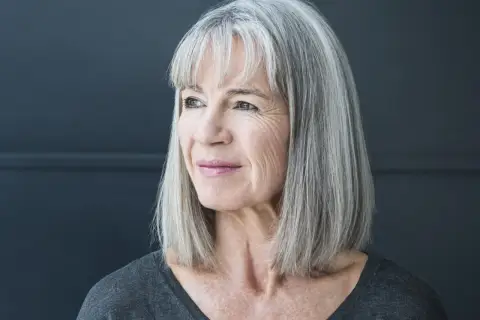 Porträt einer Frau mit stilvollen grauen Haaren, die nachdenklich zur Seite blickt.