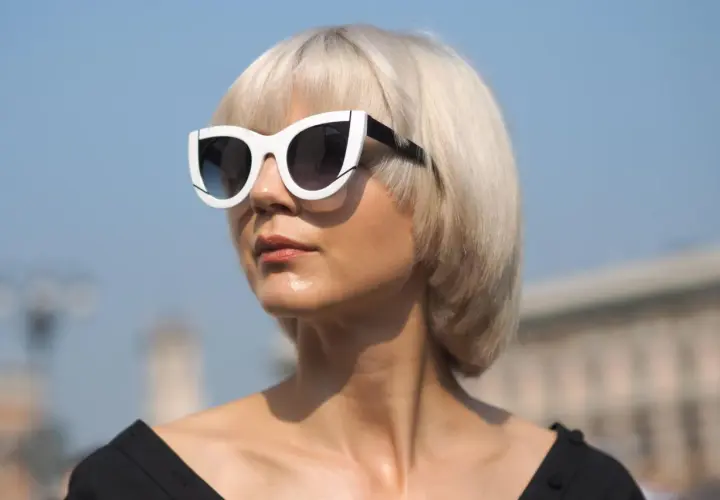 Blonde Frau mit Pagenschnitt und auffälliger Sonnenbrille blickt nach rechts.