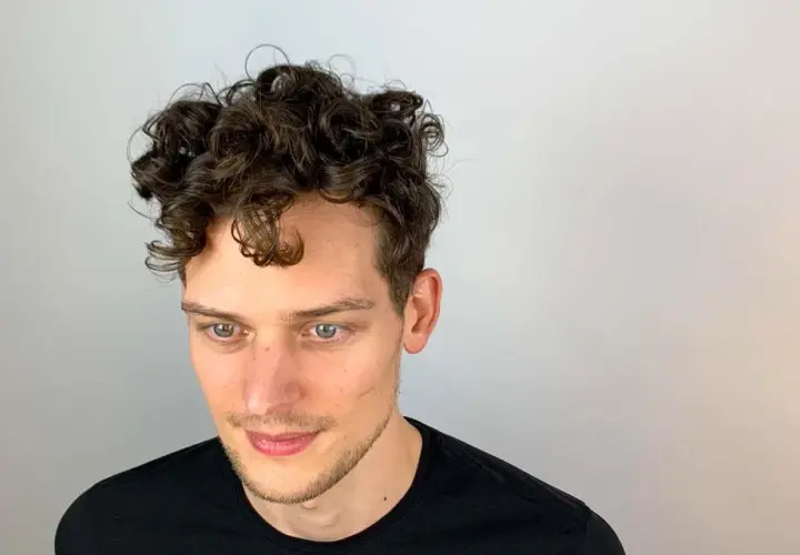 Junger Mann mit vollen, dunklen Locken. Ein Beispiel, wie bekommt man locken jungs für einen coolen Look.