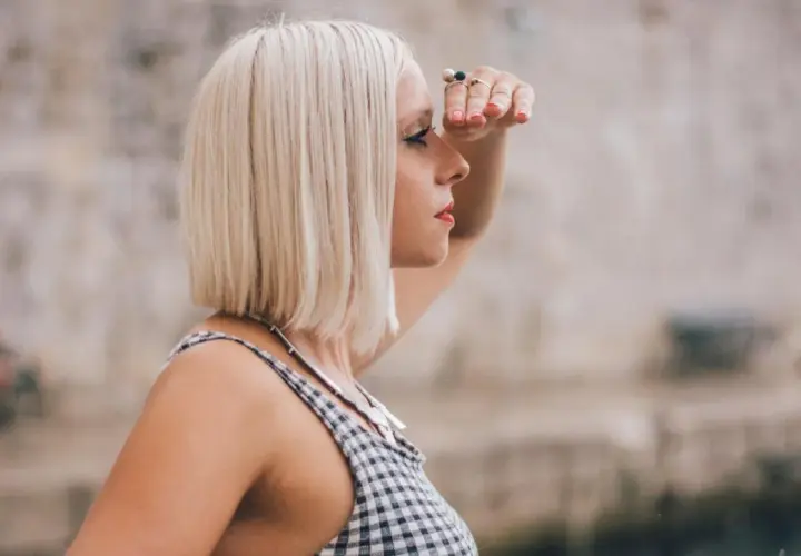 Frau mit **long bob blond** schaut in die Ferne, die Hand schützend über die Augen gelegt.