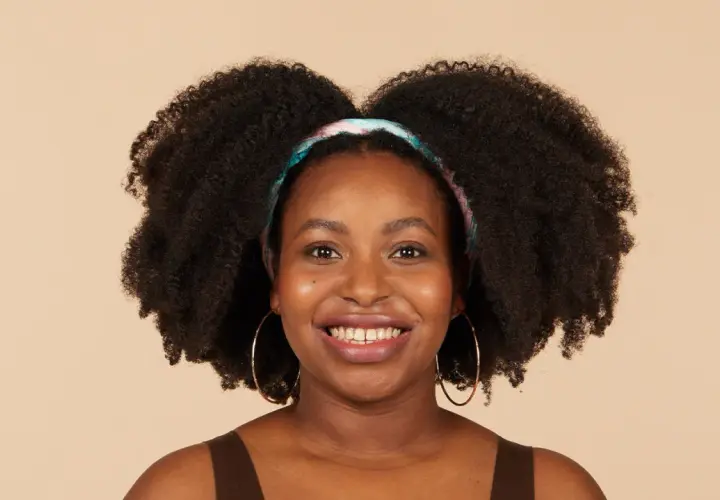 Lächelnde Frau mit voluminösen 4c Locken und einem bunten Haarband.