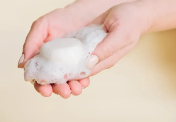 Hände halten festes Shampoo und Schaum. So einfach ist es, wie man festes Shampoo benutzt.