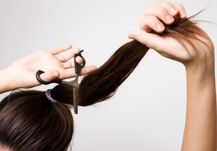 Frau schneidet sich mit einer Effilierschere die Haare, um einen Stufenschnitt selber zu schneiden.