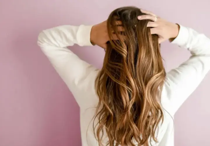 Frau mit langen, welligen 2a Haaren, die sie mit den Händen im Nacken hält.