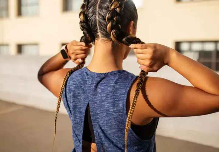 Sportliche Frau mit boxer braids, die ihre Zöpfe zurechtrückt.