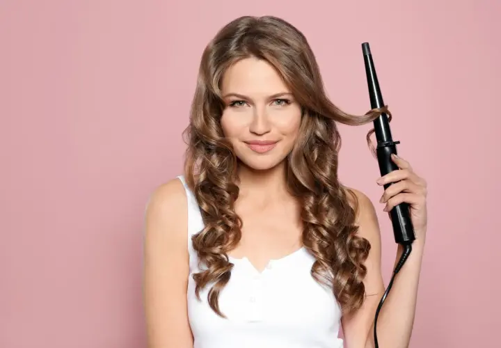 Frau mit braunen Haaren, die mit einem Lockenstab ihre Locken definiert.
