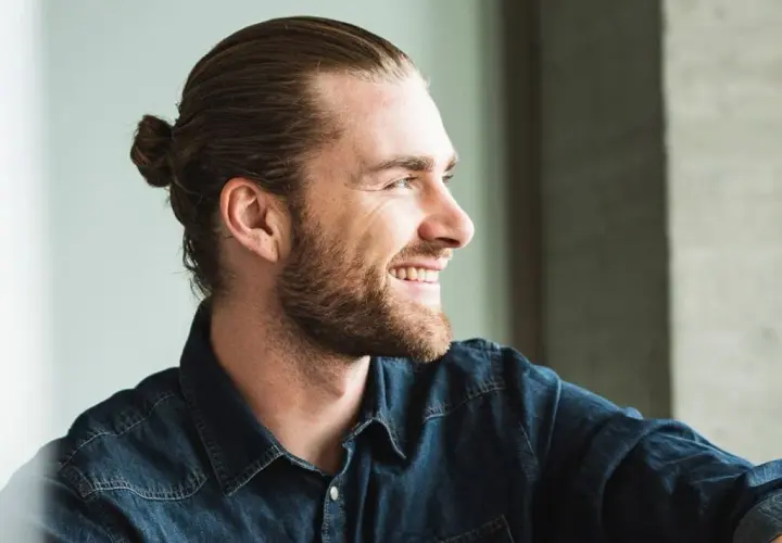 Lächelnder Mann mit Bart und einem lässigen **man bun** im Jeanshemd.
