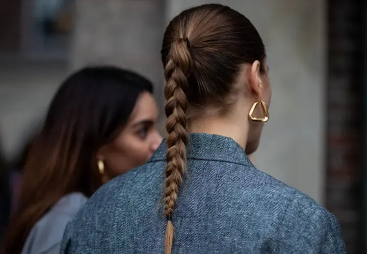 Eine Frau mit geflochtenen Haaren trägt einen grauen Blazer und auffällige goldene Ohrringe.