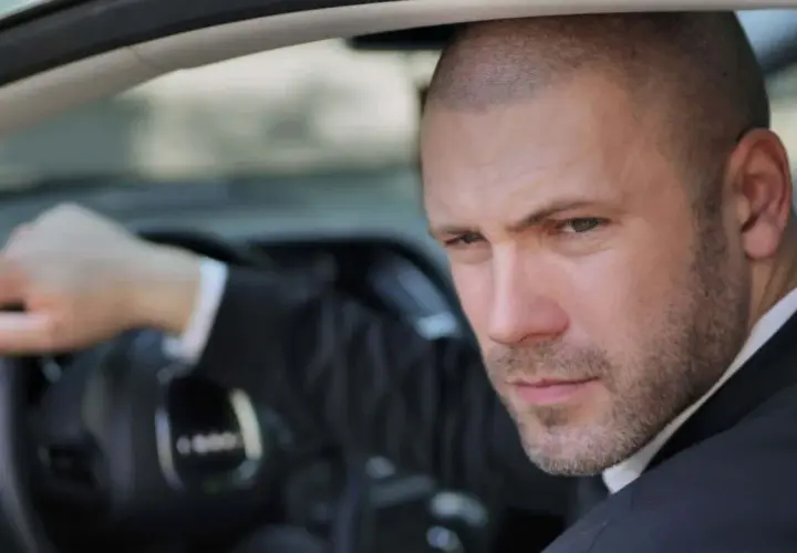 Mann mit Buzz Cut Mid Fade im Anzug fährt Auto.